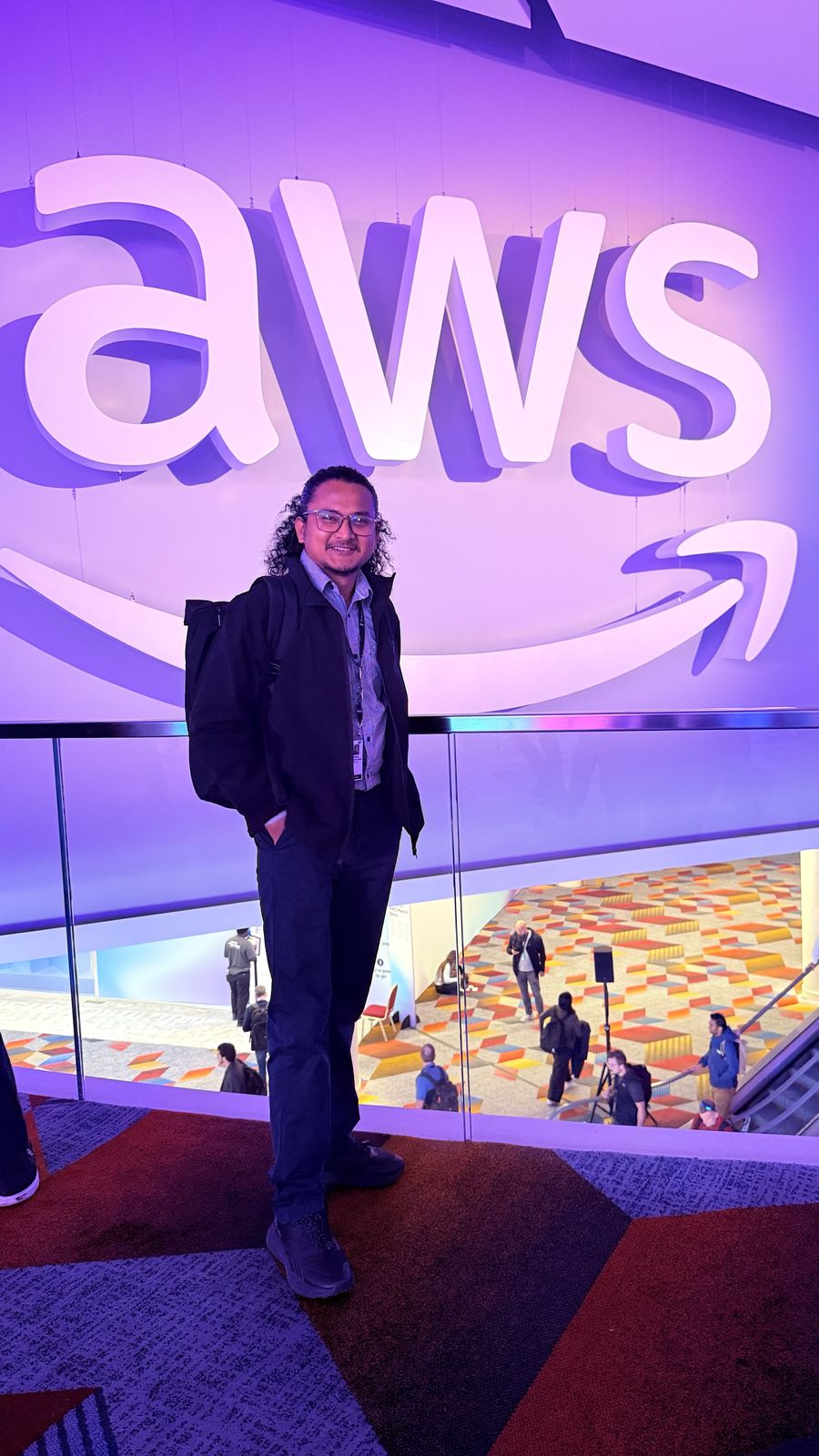 Hikmat standing beneath a large illuminated AWS logo at a conference