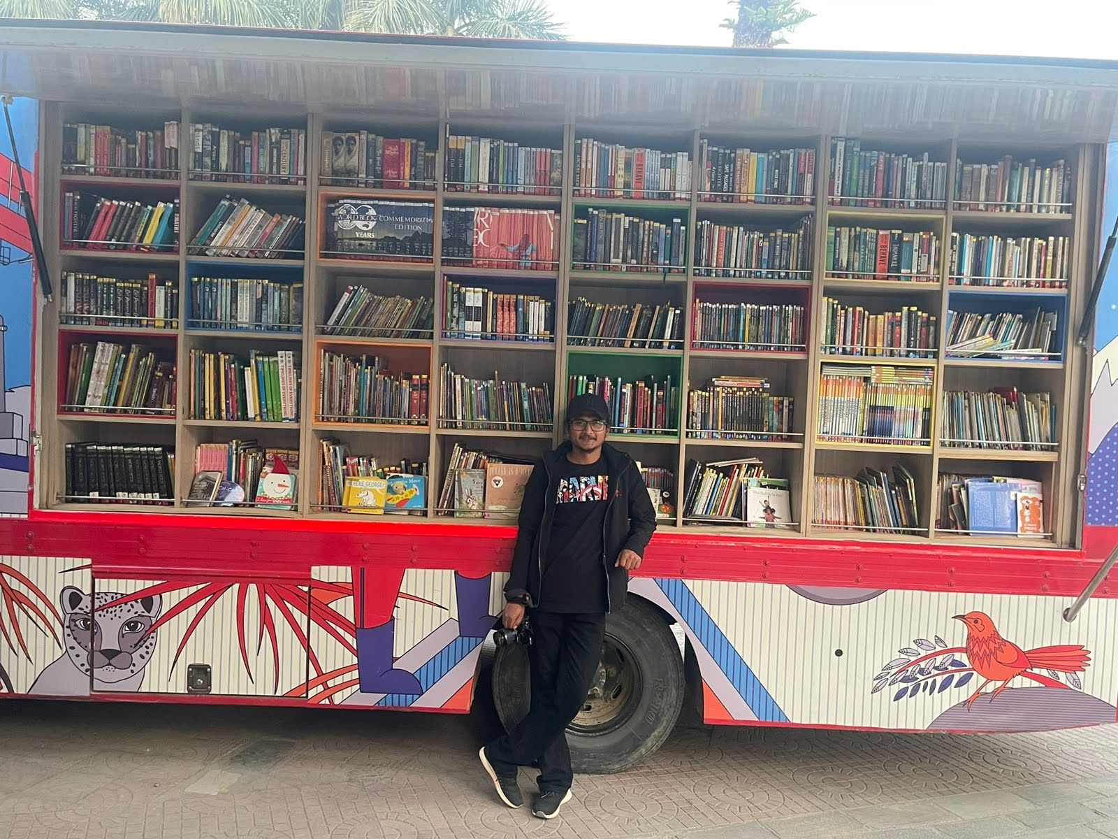 Hikmat leaning against a colourful mobile library bus filled with books