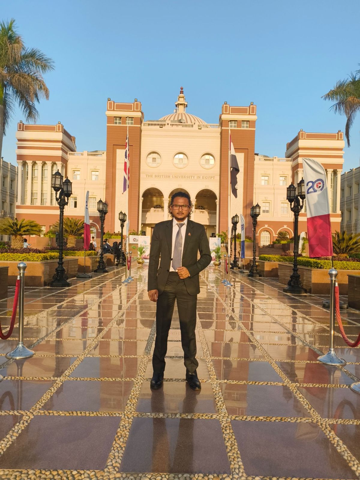 Hikmat in a suit standing in front of the British University in Egypt