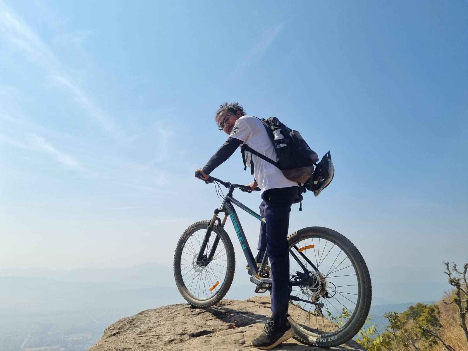 Hikmat on a mountain bike at the edge of a rocky viewpoint under a blue sky