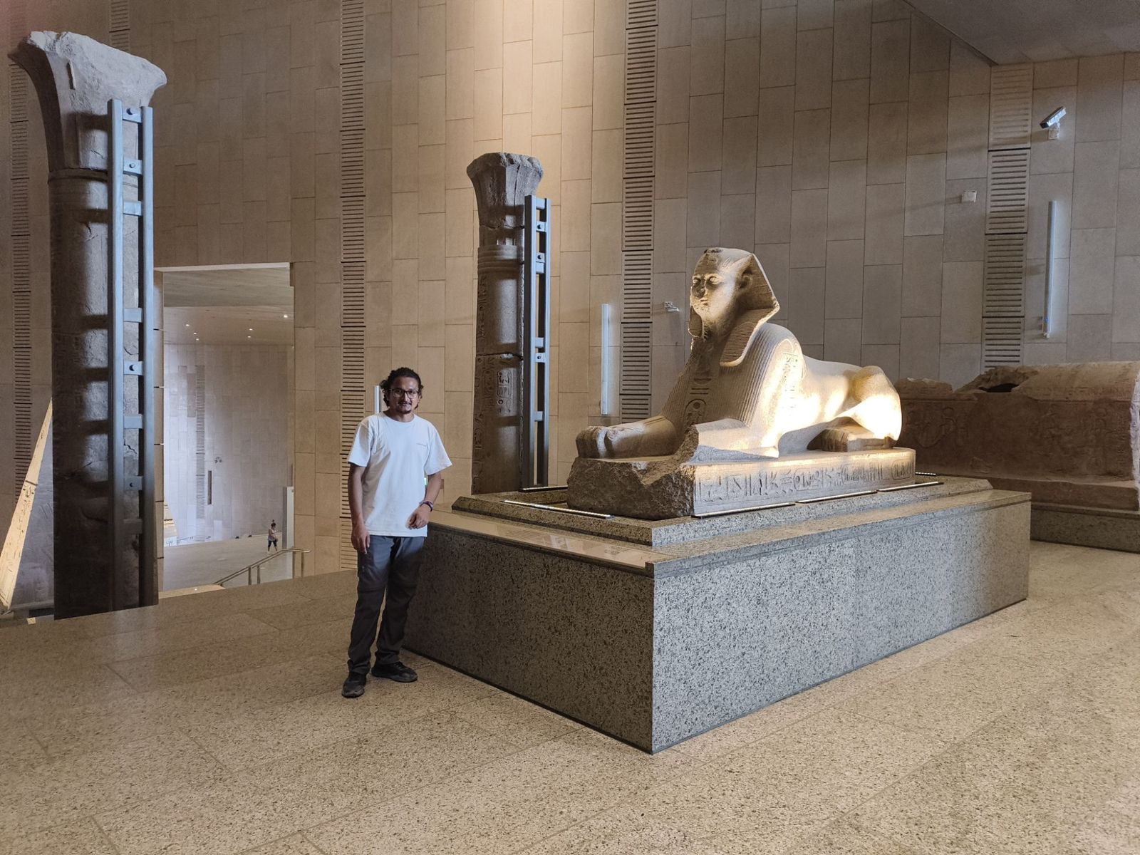 Hikmat standing beside a large granite sphinx inside a museum hall