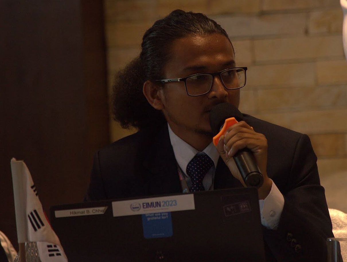 Hikmat speaking into a microphone in a committee session
